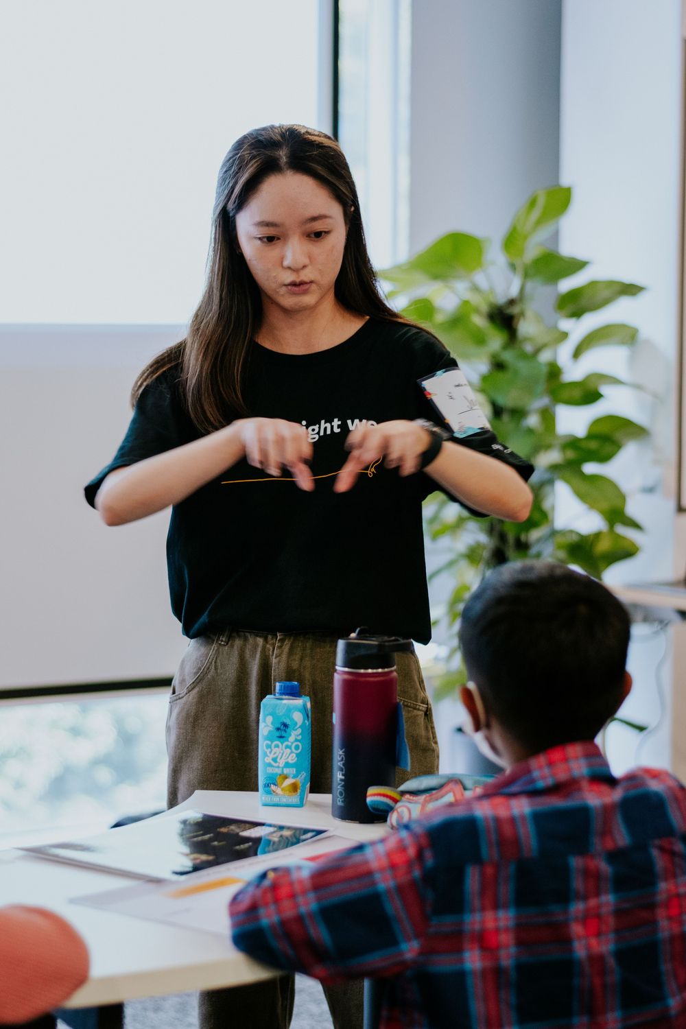 Students collaborate at a desk with reusable water bottles and a houseplant in the background of a modern workspace.