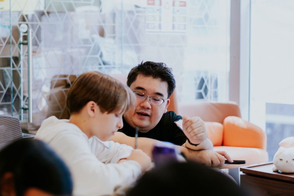 Students work together at shared tables in a bright modern classroom setting.
