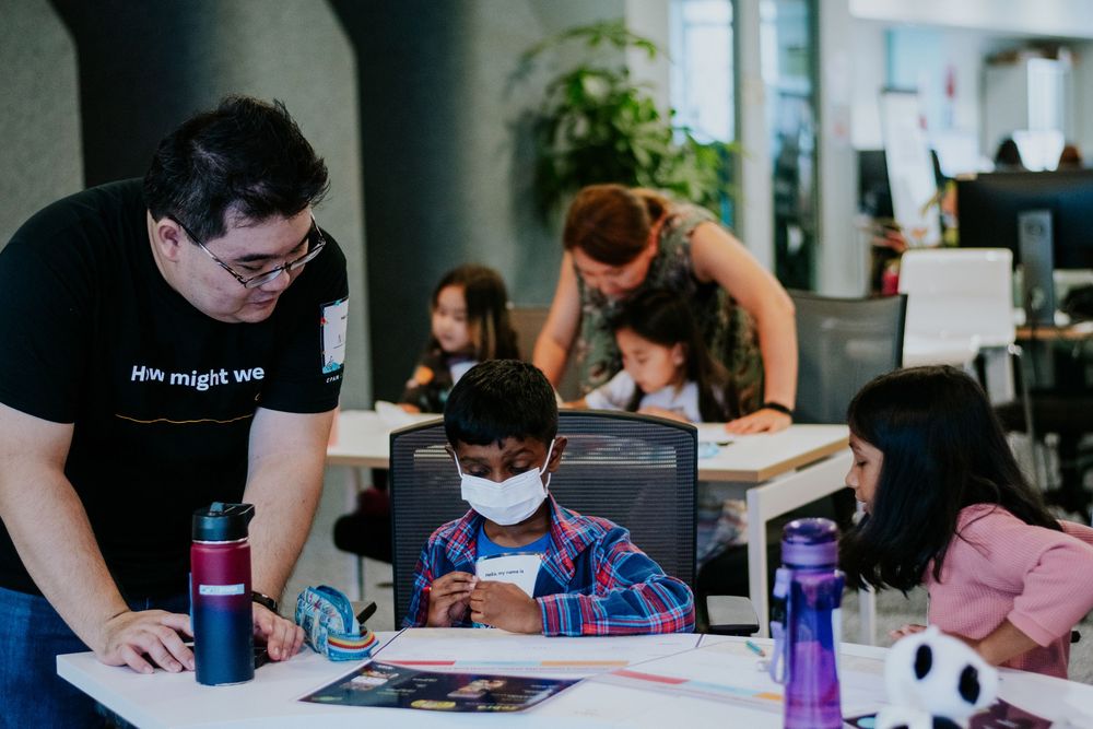 Students work diligently at desks with purple water bottles and study materials in a modern office setting.