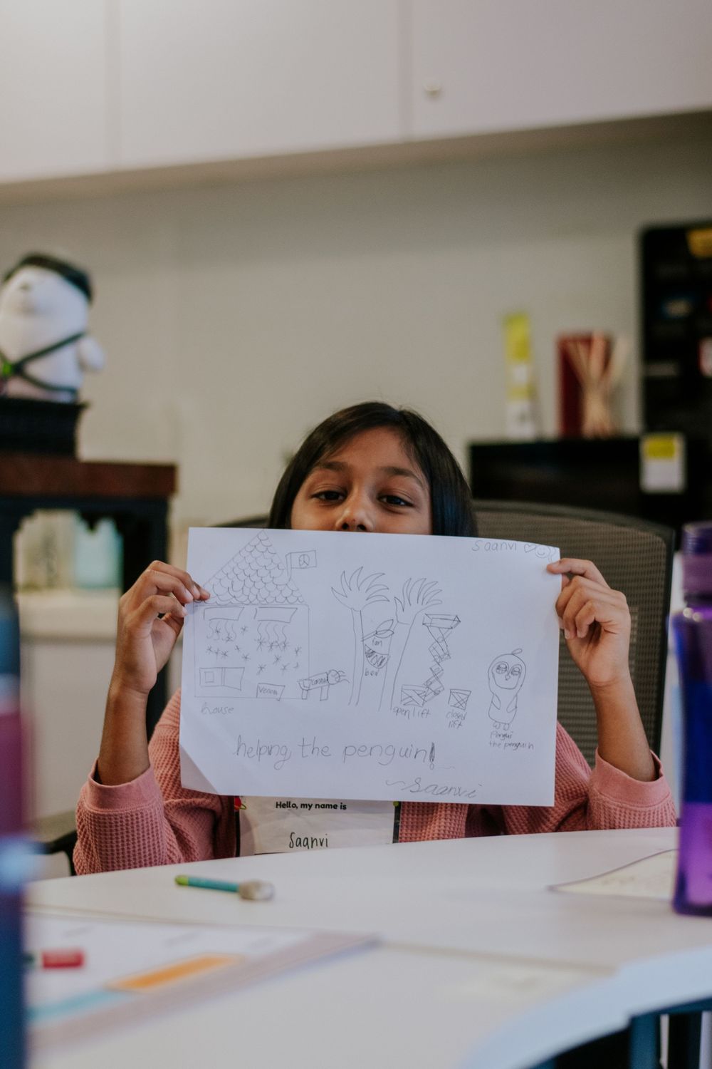 Student shows off their pencil drawing artwork at a desk with school supplies scattered around.