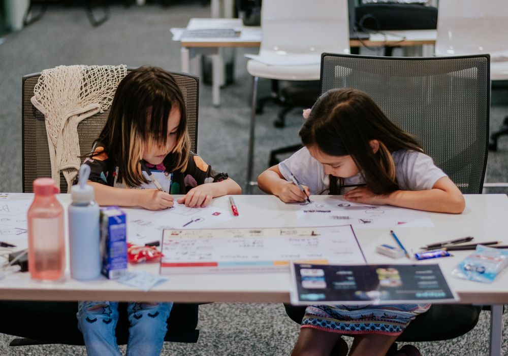 Students work diligently at desks with papers and school supplies in a classroom setting.