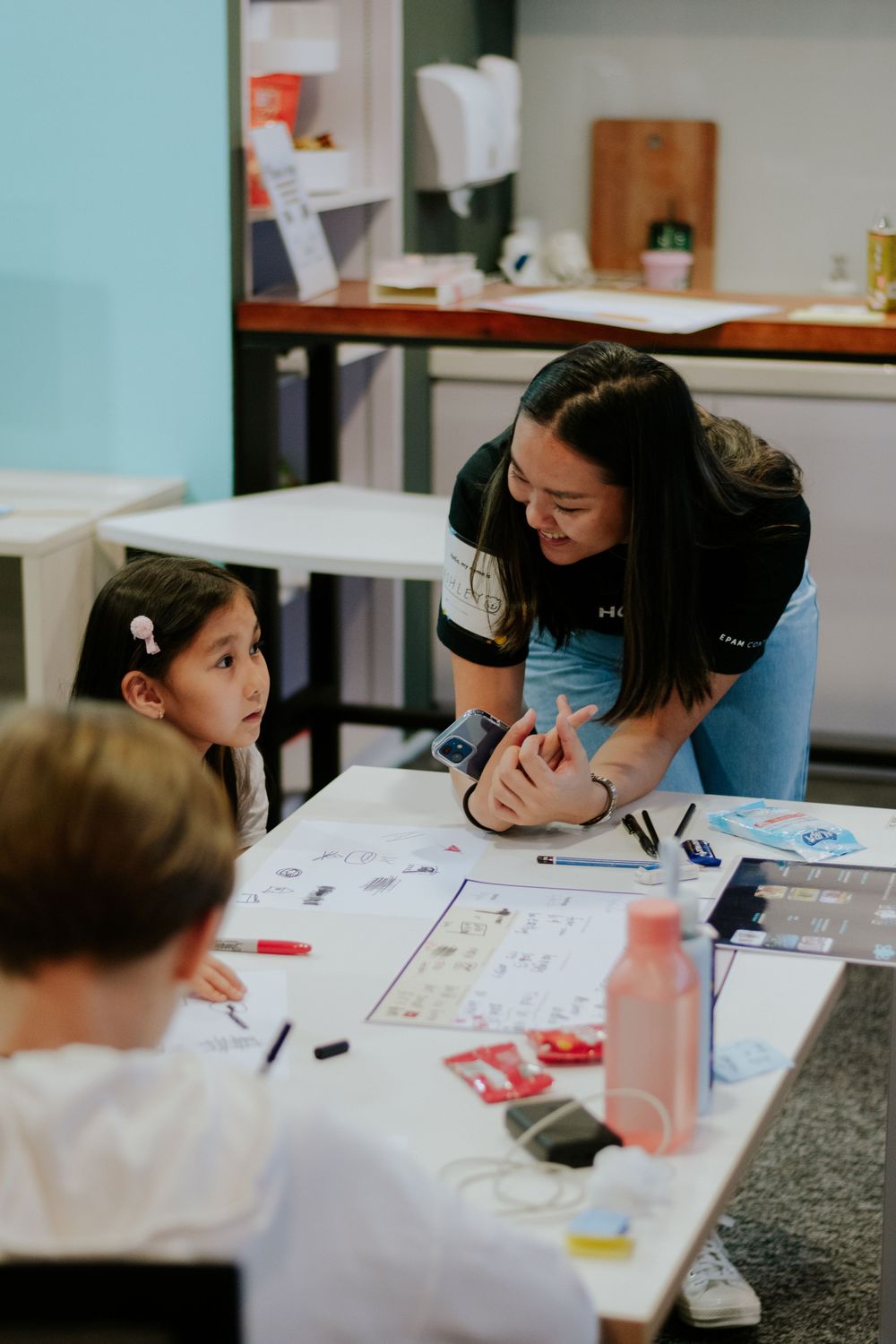 Students work together at a desk while receiving guidance from a teacher in a classroom setting.