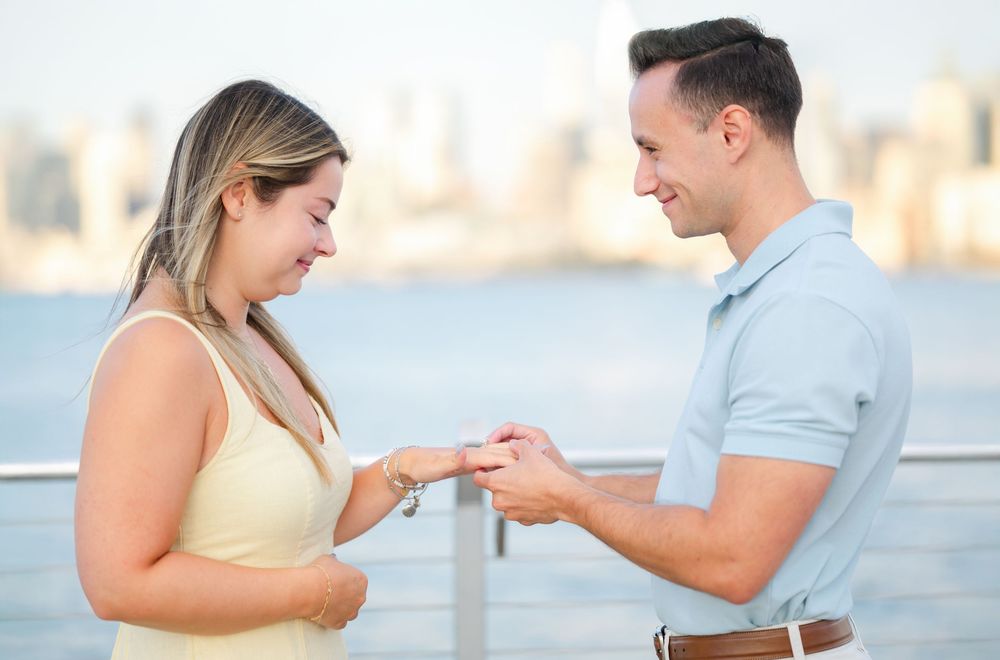 Couple sharing emotional engagement moment against NYC waterfront during golden hour.