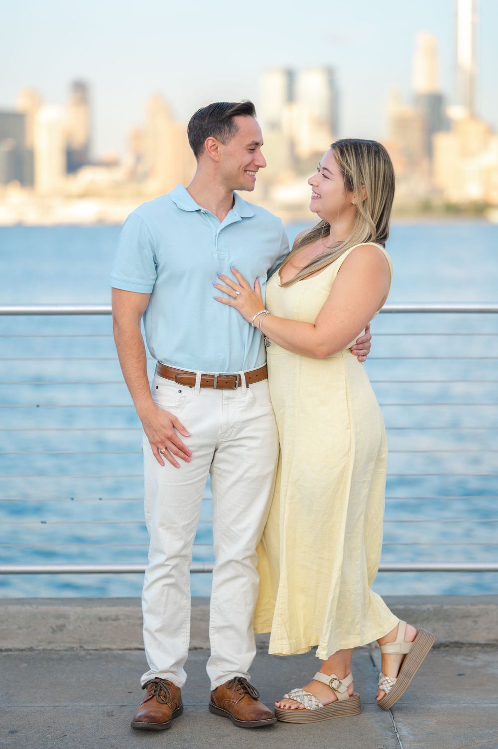 Couple celebrating engagement on pier with city skyline visible across the water.