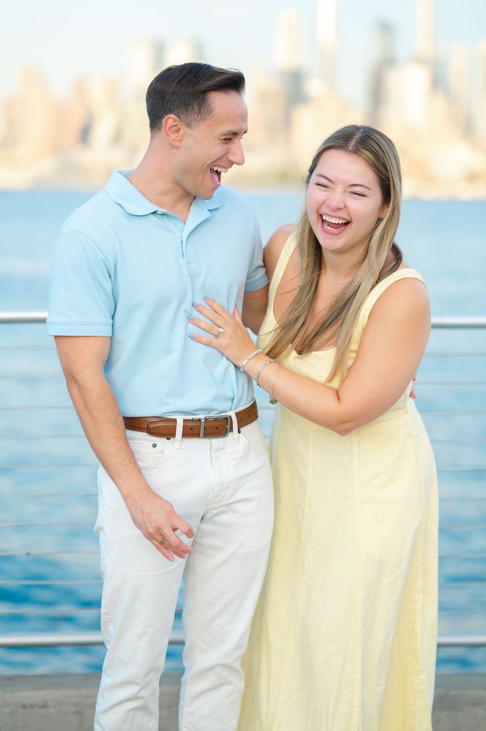 A couple shares a joyful moment by the waterfront wearing coordinated light blue and yellow summer outfits during their proposal session.