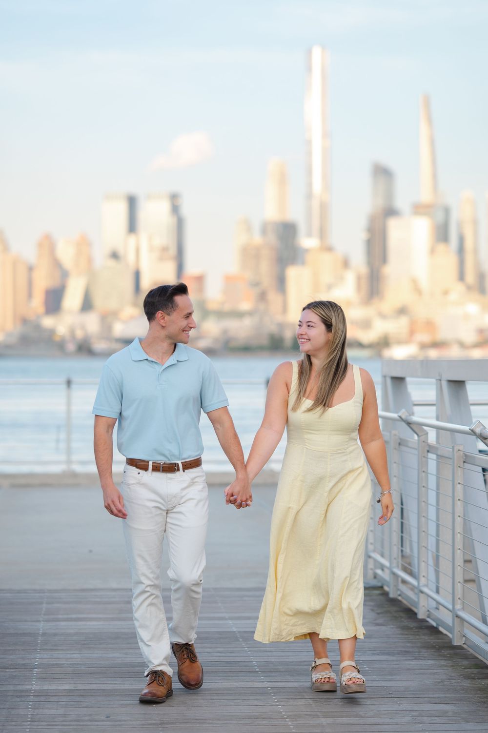 A couple strolls together on a pier in NJ during golden hour with Manhattan's skyline creating a romantic backdrop after their engagement.