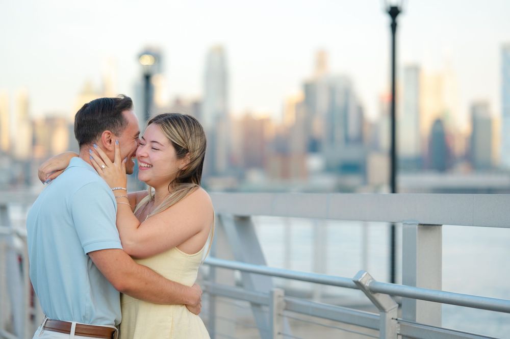 Couple embraces on waterfront deck with city skyline view at sunset.