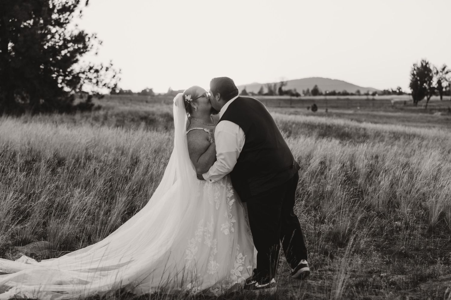 A romantic black and white wedding photo sequence showing a couple embracing in a grassy field at sunset.