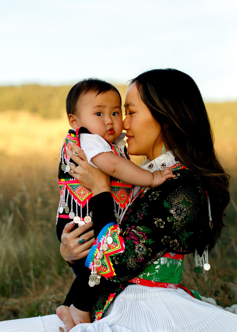 Mother and child share an intimate moment together in traditional dress against a golden sunset field in Missoula