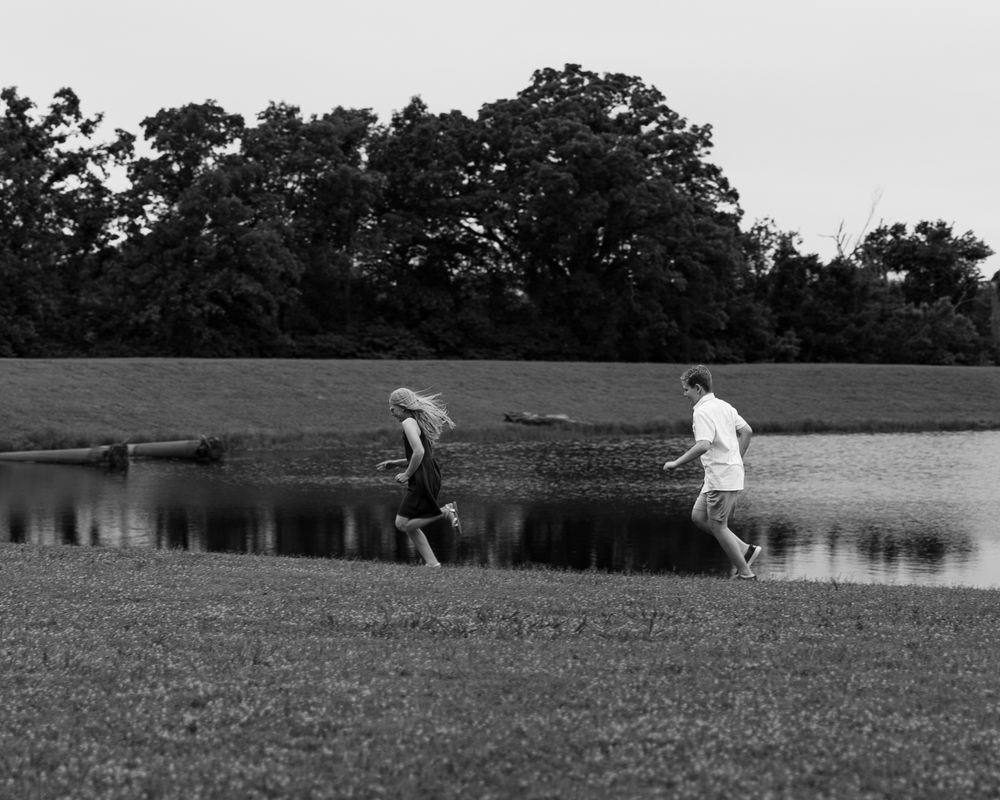 Playful family photography in Missoula shows brother and sister run outside next to pond taken by Shawn Strasburg Photography