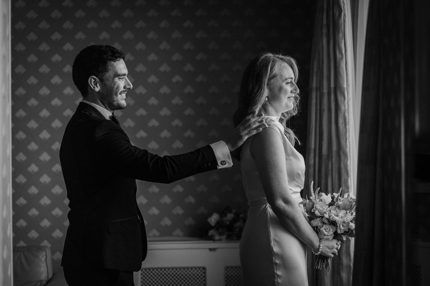 Black and white artistic wedding photo with elegant wallpaper backdrop.