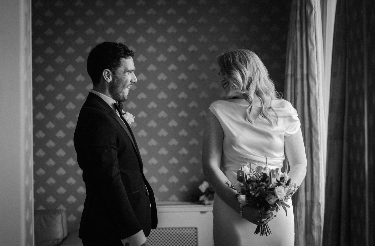 Intimate black and white wedding moment captured against patterned wallpaper.