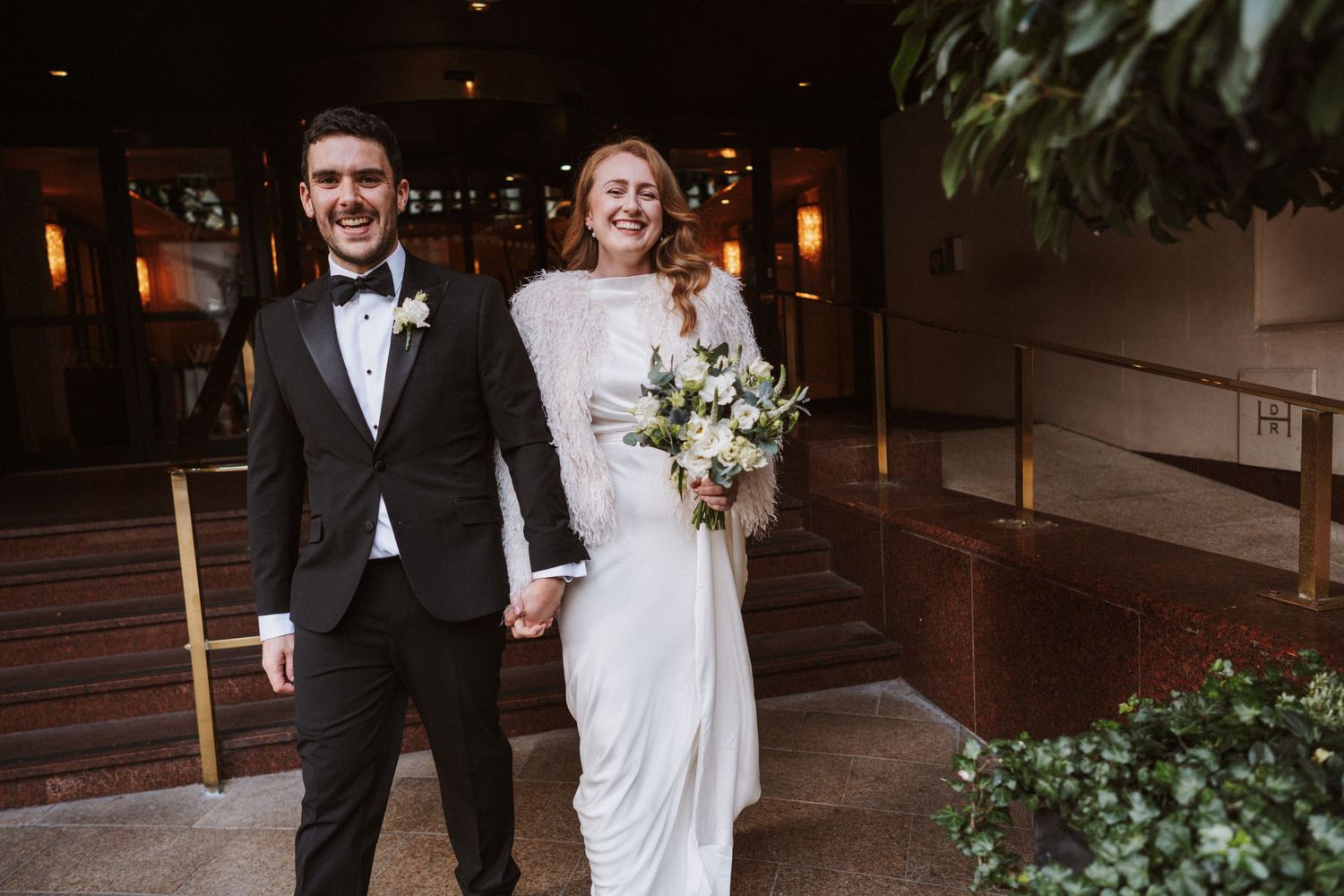 A couple in wedding attire shares a romantic moment while walking together in an outdoor setting.