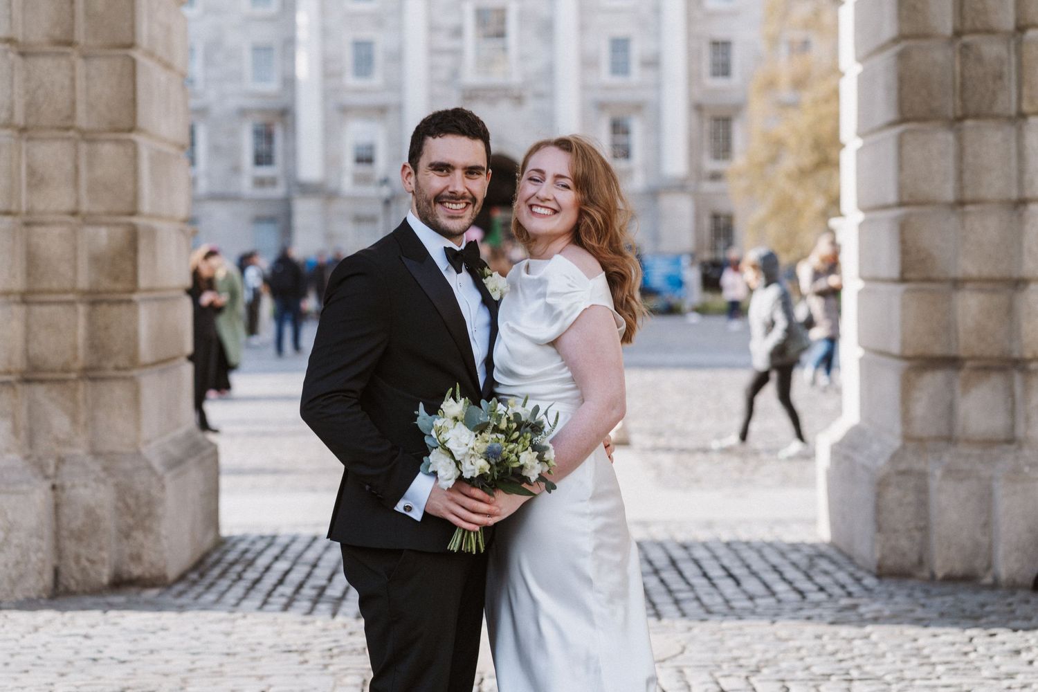 Newlyweds share intimate moment under stone archway of historic building.