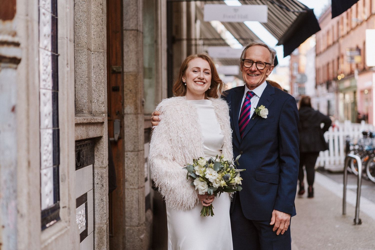 Wedding couple laughs together while walking through historic stone colonnade.