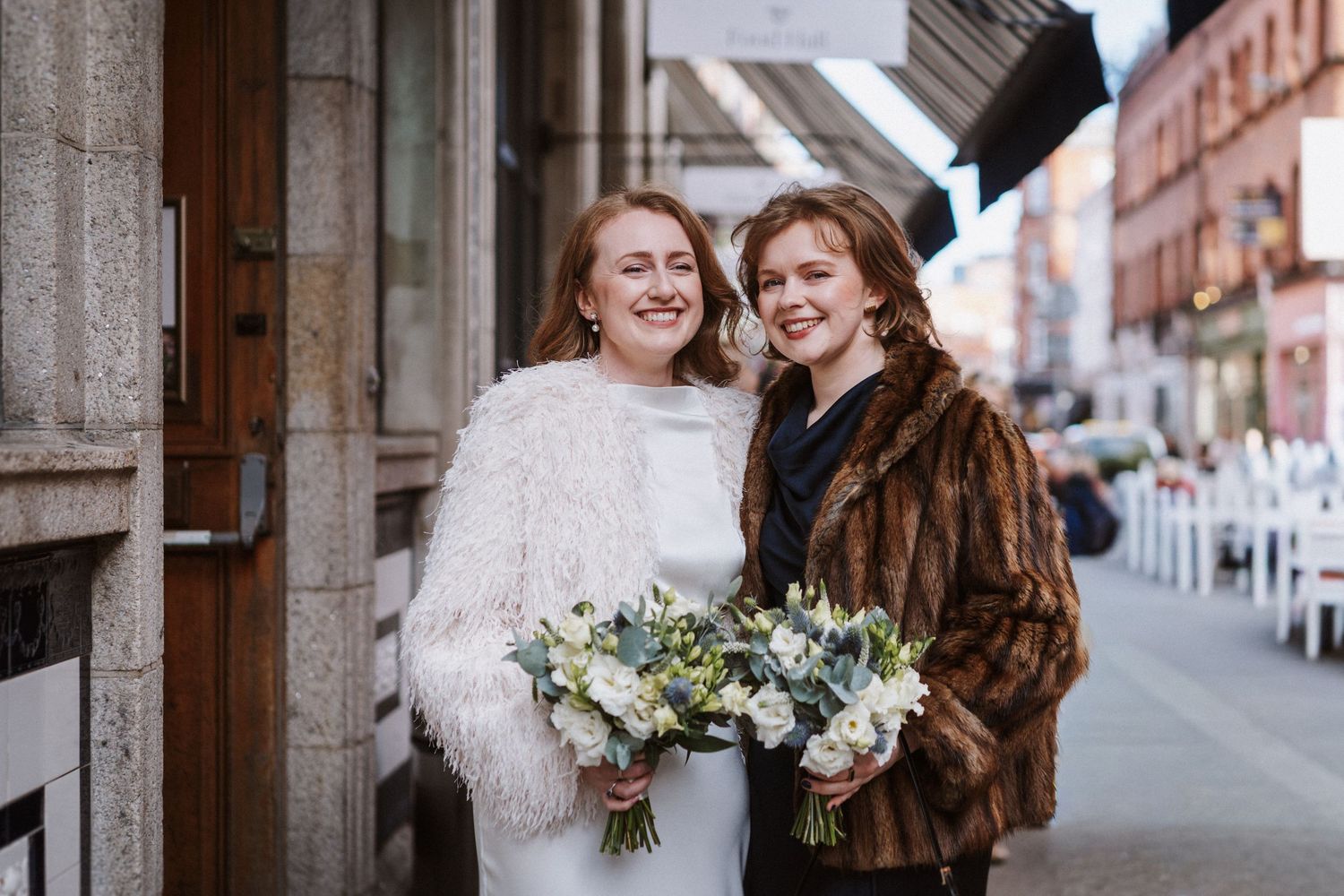 Two people in winter wedding attire share a joyful moment together on a city street.