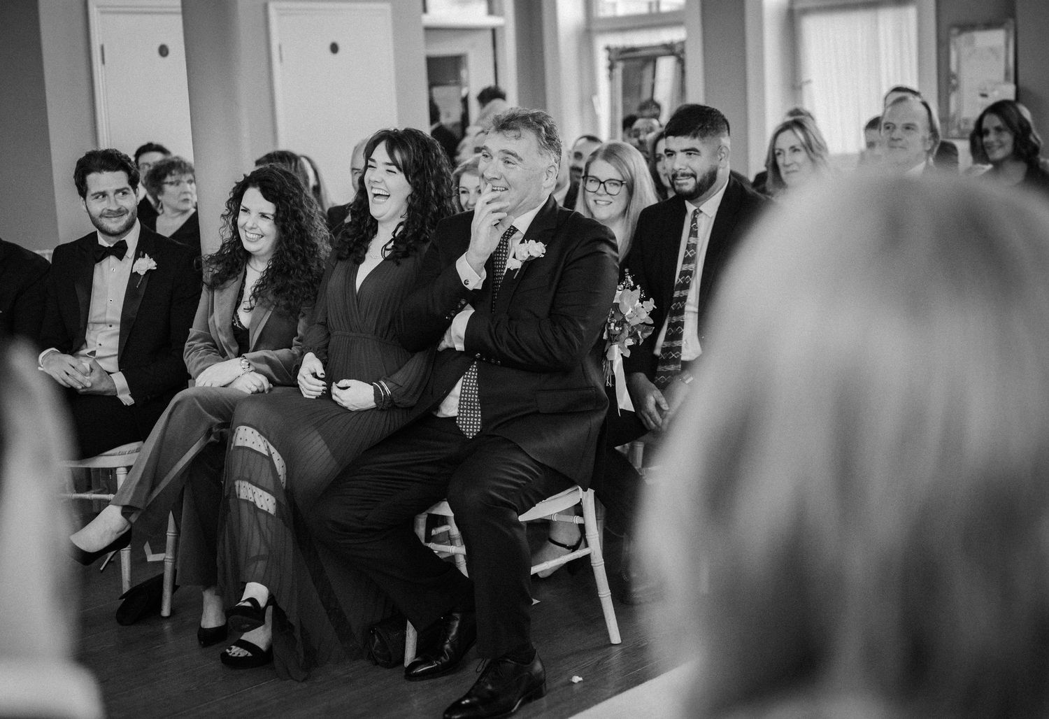 Black and white photo of wedding guests seated in rows during a ceremony, watching attentively.