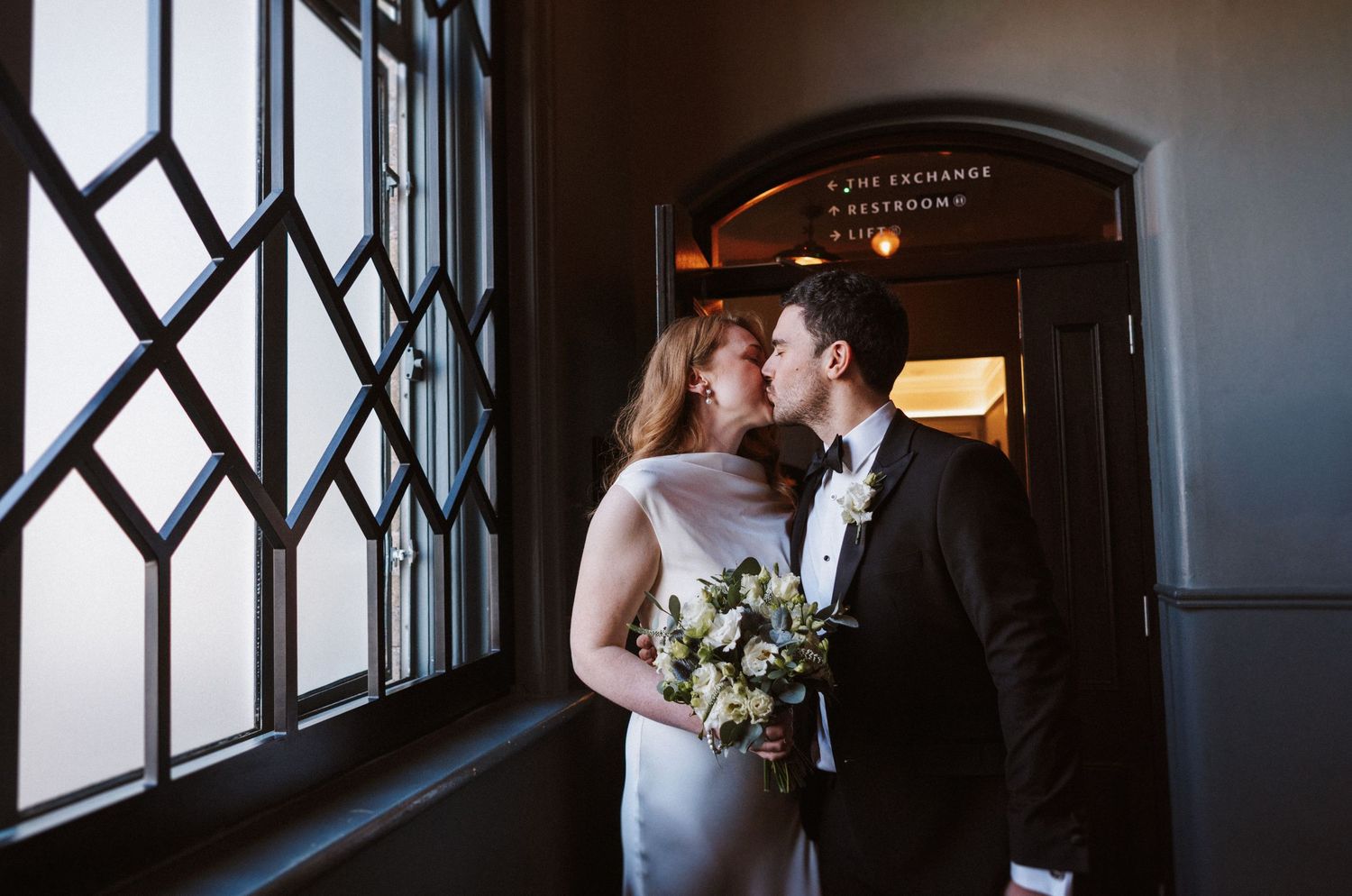Dramatic window lighting silhouettes wedding party members in an elegant indoor venue.