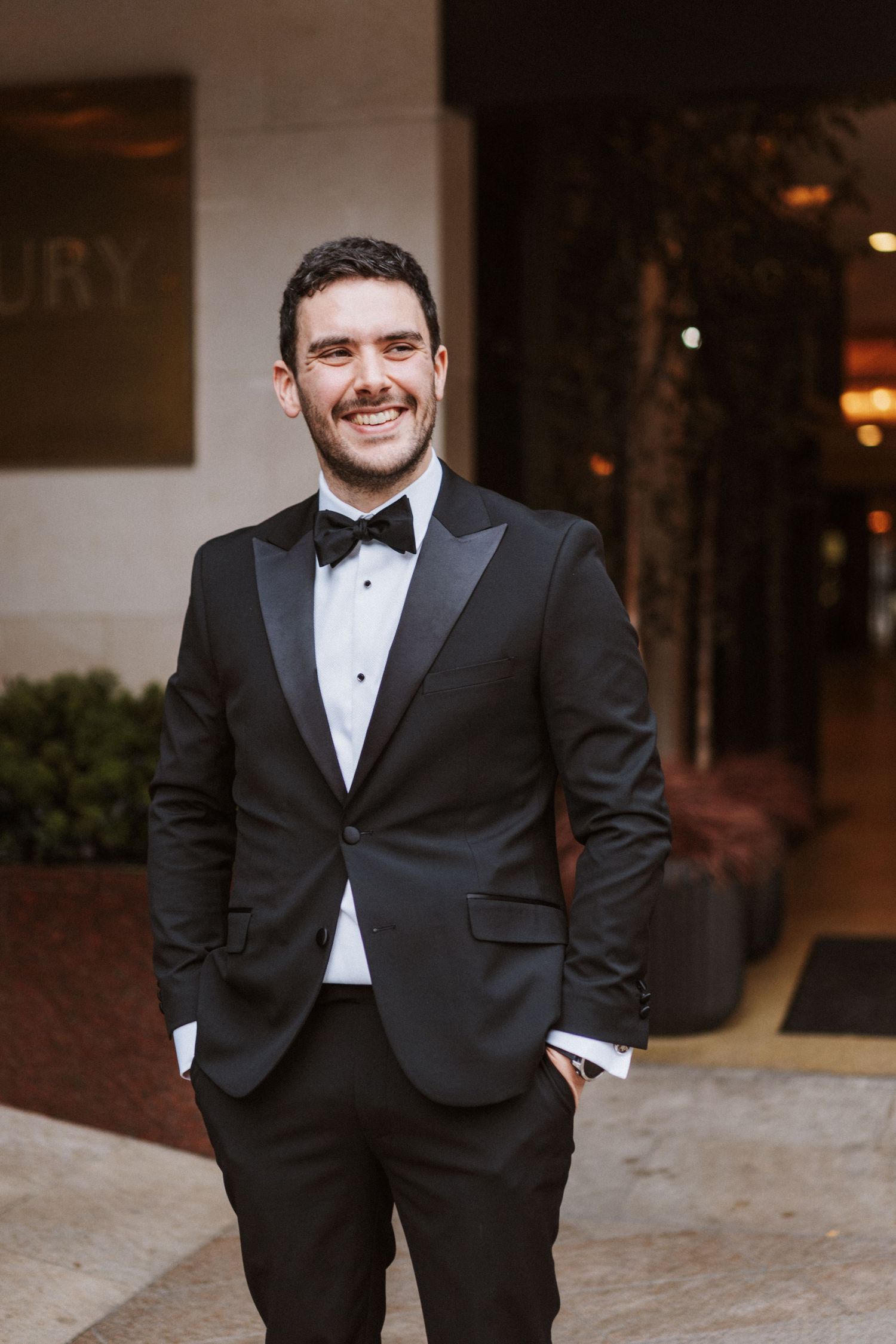 Groom in classic black tuxedo and bowtie poses during formal wedding portraits.