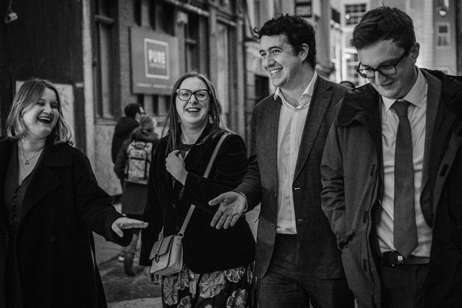 Black and white photo of wedding guests socializing outside on an urban street.