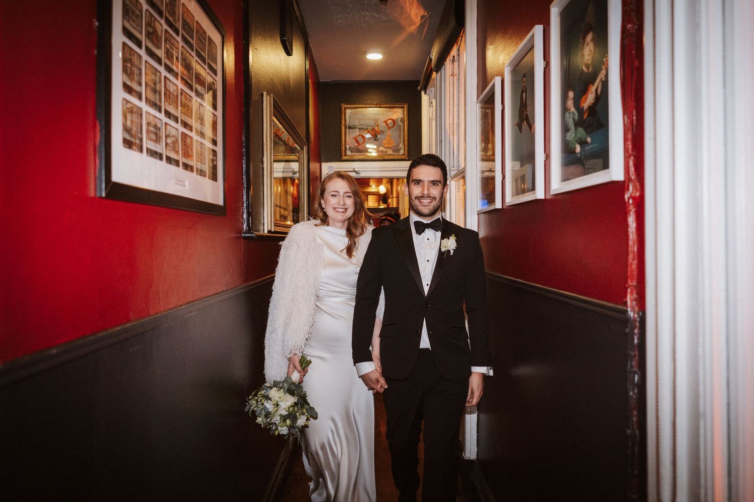 Wedding couple photographed in dramatic red-walled hallway with bright lighting and modern decor.