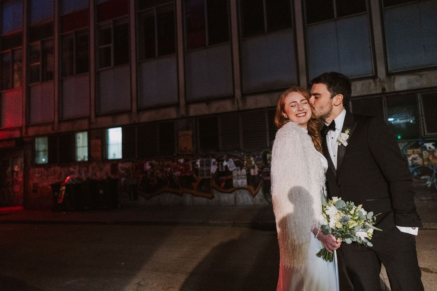 Newlyweds share a romantic kiss under moody evening lighting at their wedding reception.