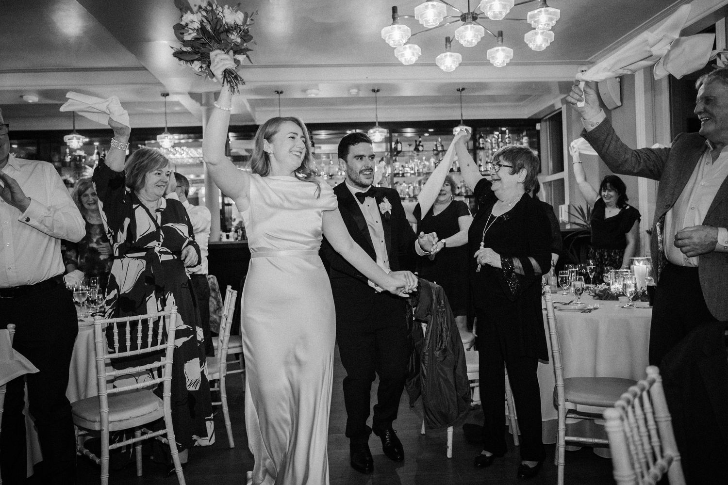 Wedding reception venue features elegant chandeliers and white decor as guests celebrate on the dance floor.