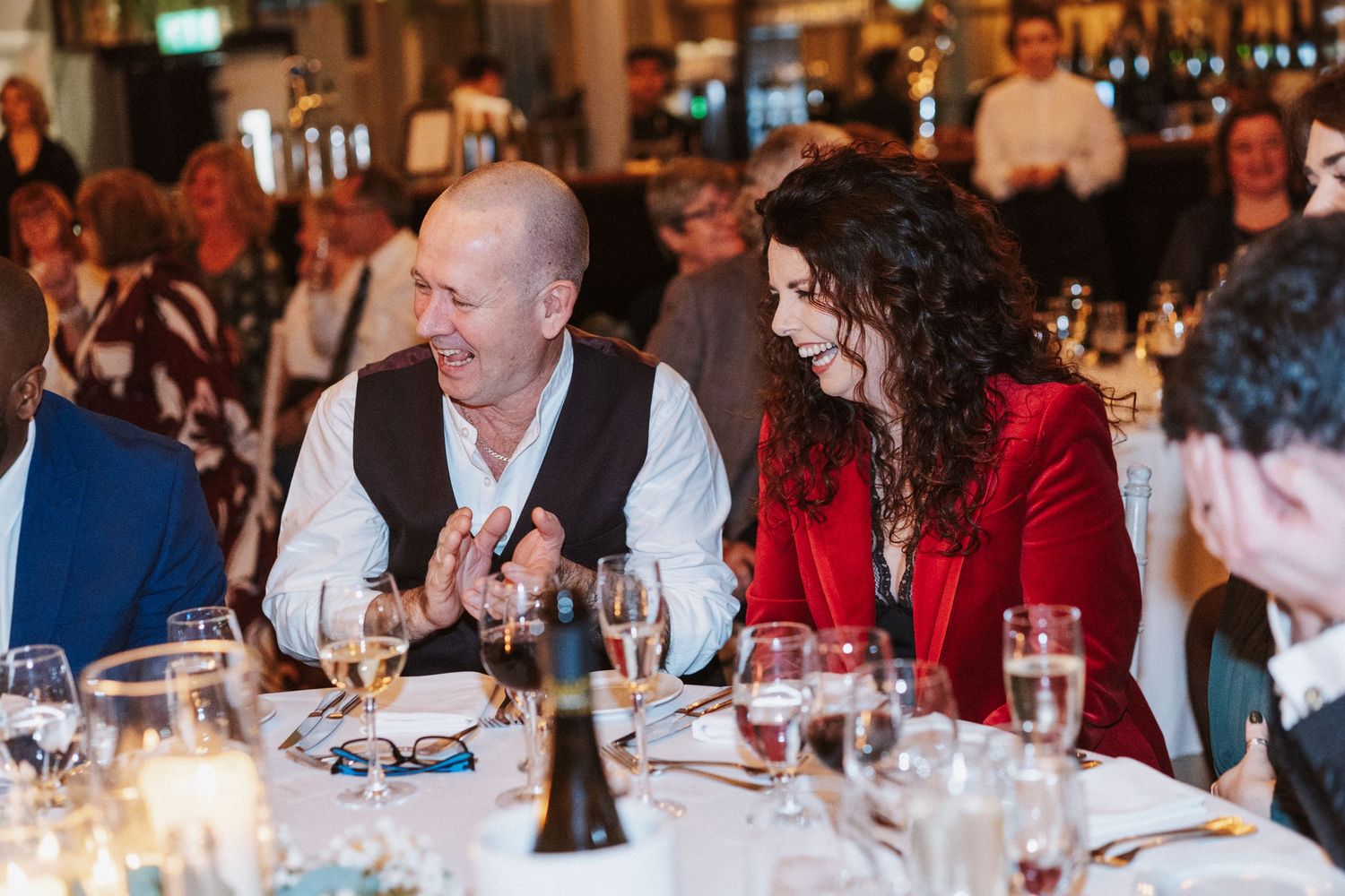 Wedding guests enjoy dinner and conversation at elegantly set reception tables with candlelight.