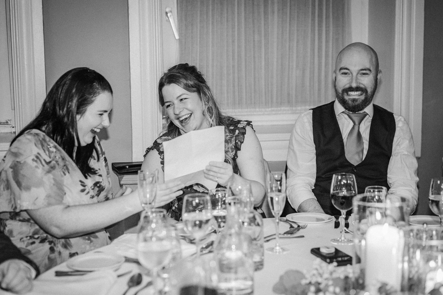 Wedding guests enjoying dinner and conversation at an elegant reception table with wine glasses and candlelight.
