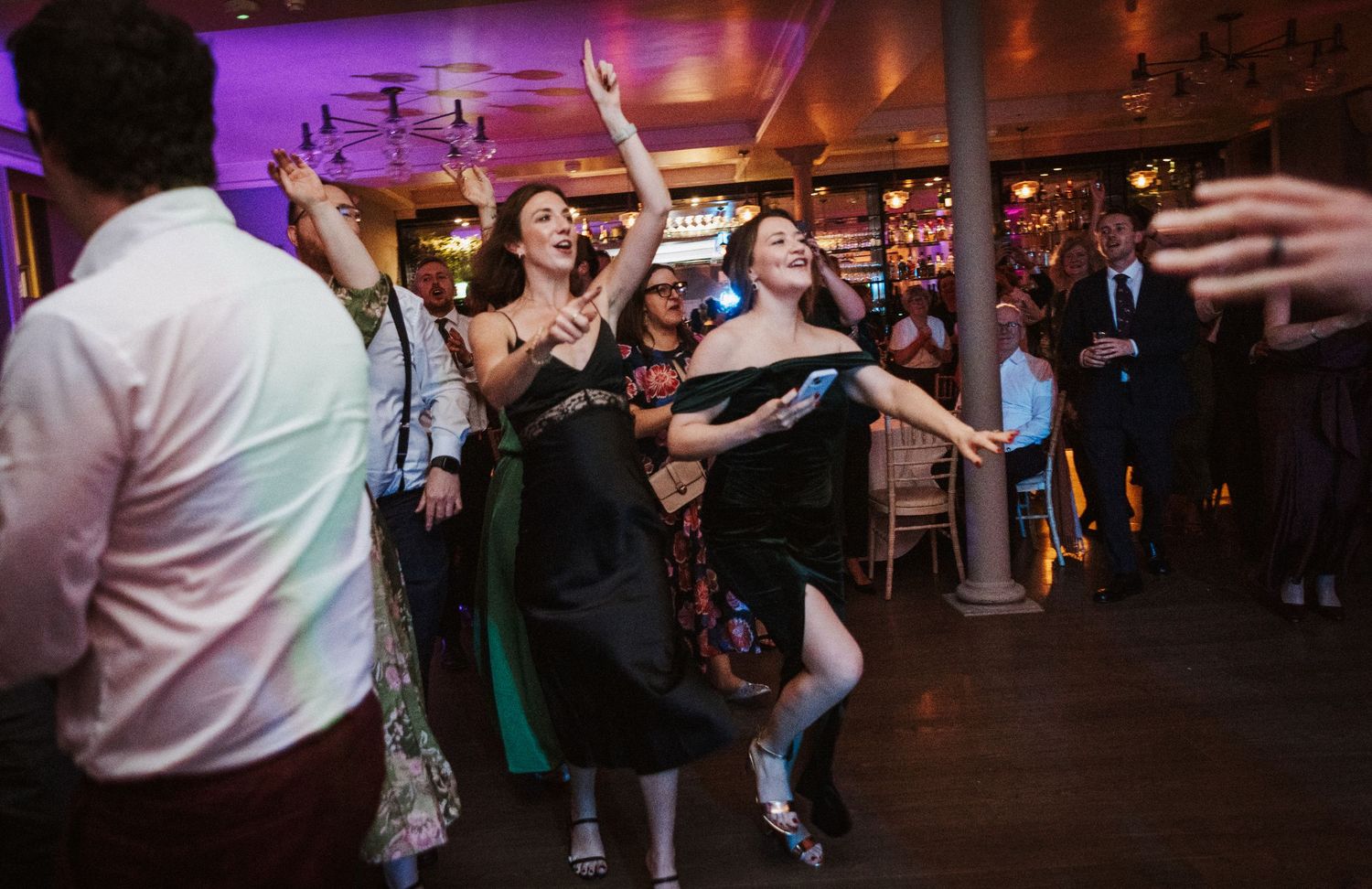 Wedding reception dance floor illuminated with purple lighting as guests dance and celebrate.