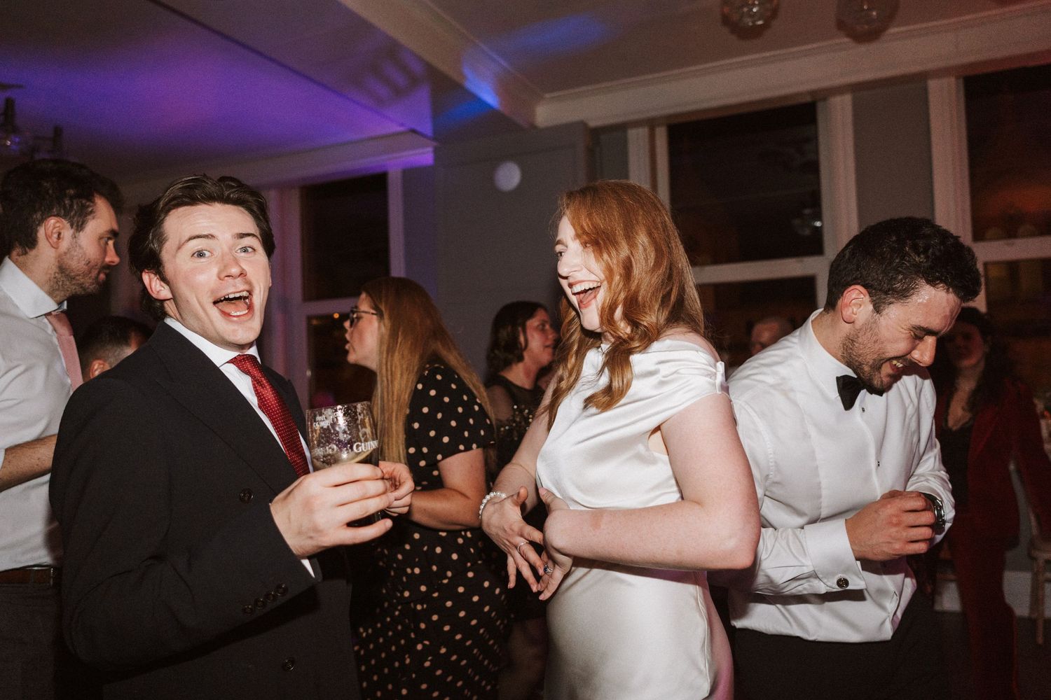 Wedding reception guests enjoying themselves on a dance floor illuminated by purple and blue lights.