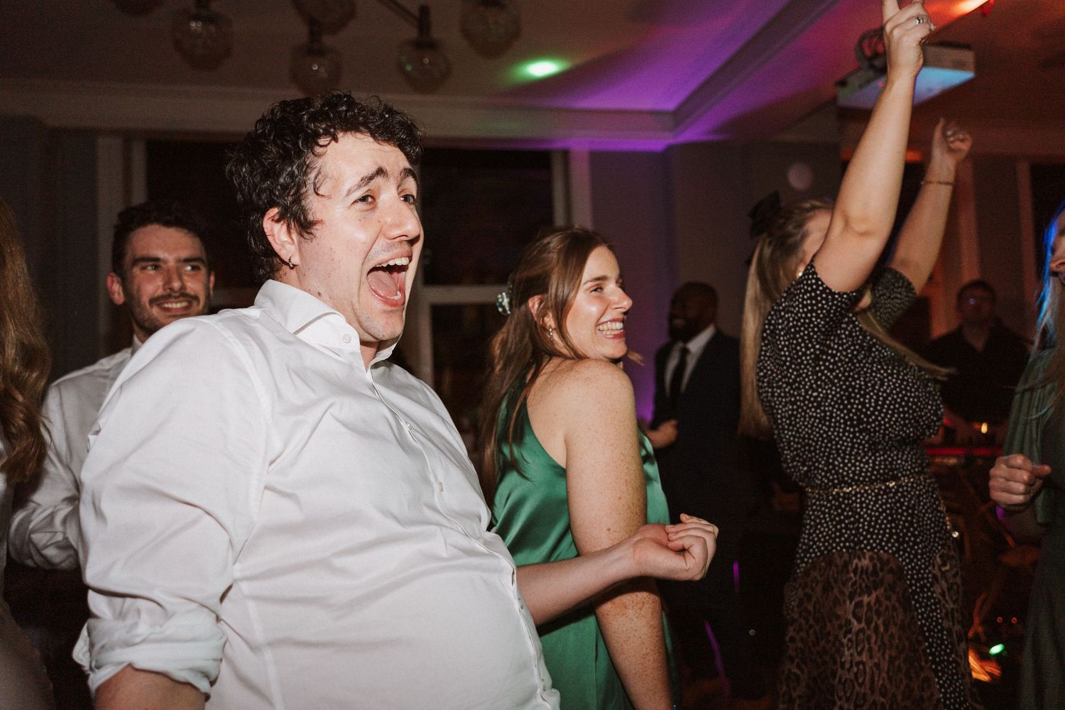 Wedding reception dance floor filled with guests enjoying themselves under purple mood lighting.