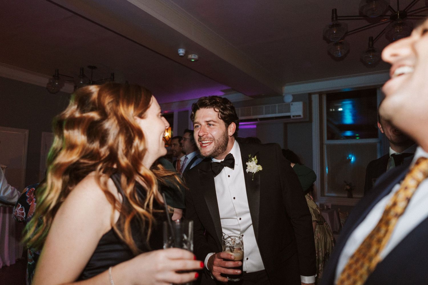 Wedding reception party guests dancing and celebrating in a dimly lit venue.