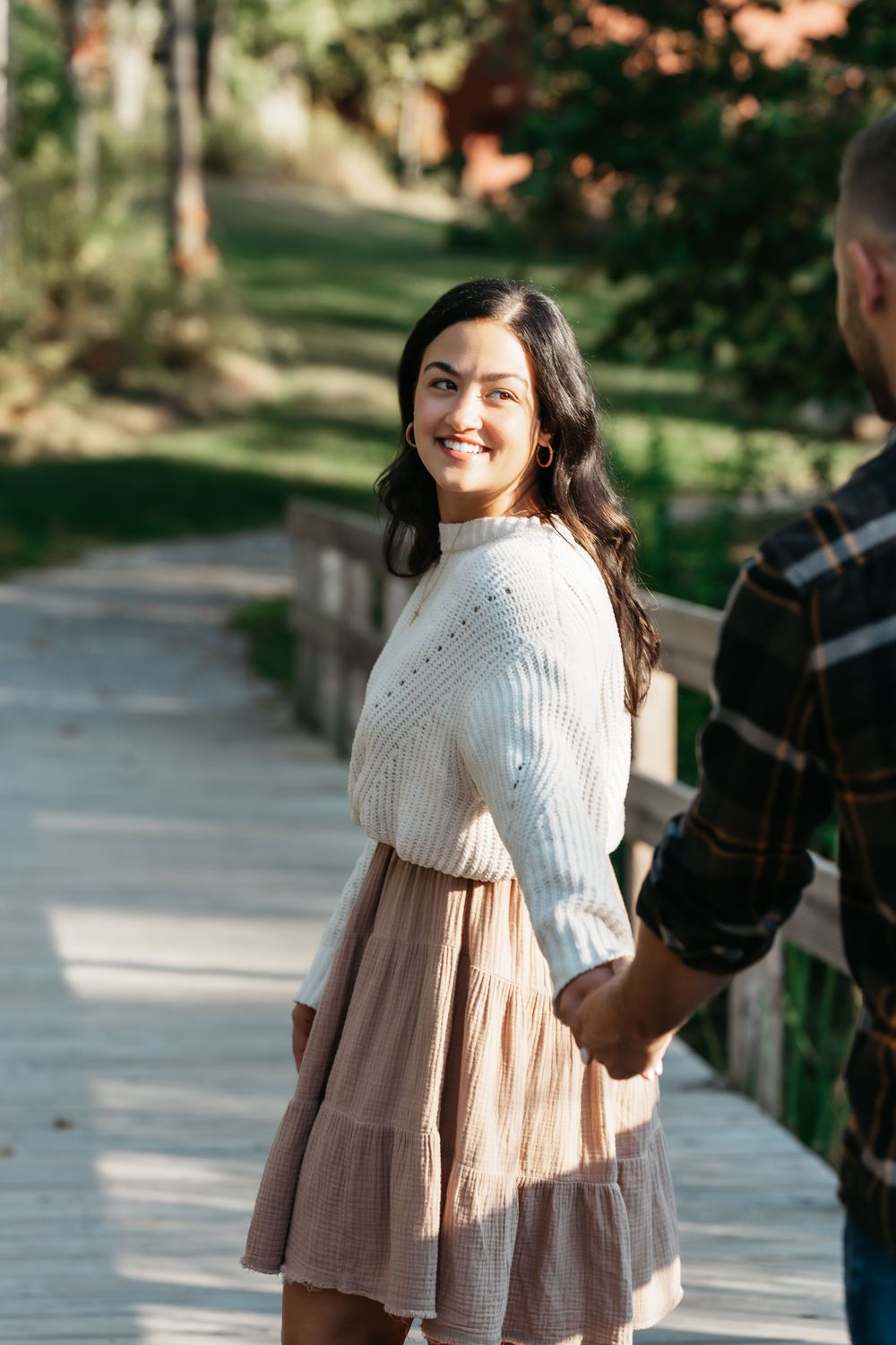 A person wearing a cream knit sweater and flowing beige skirt poses outdoors in a park setting at Mud Brook Greenway in Cuyahoga Falls, Ohio