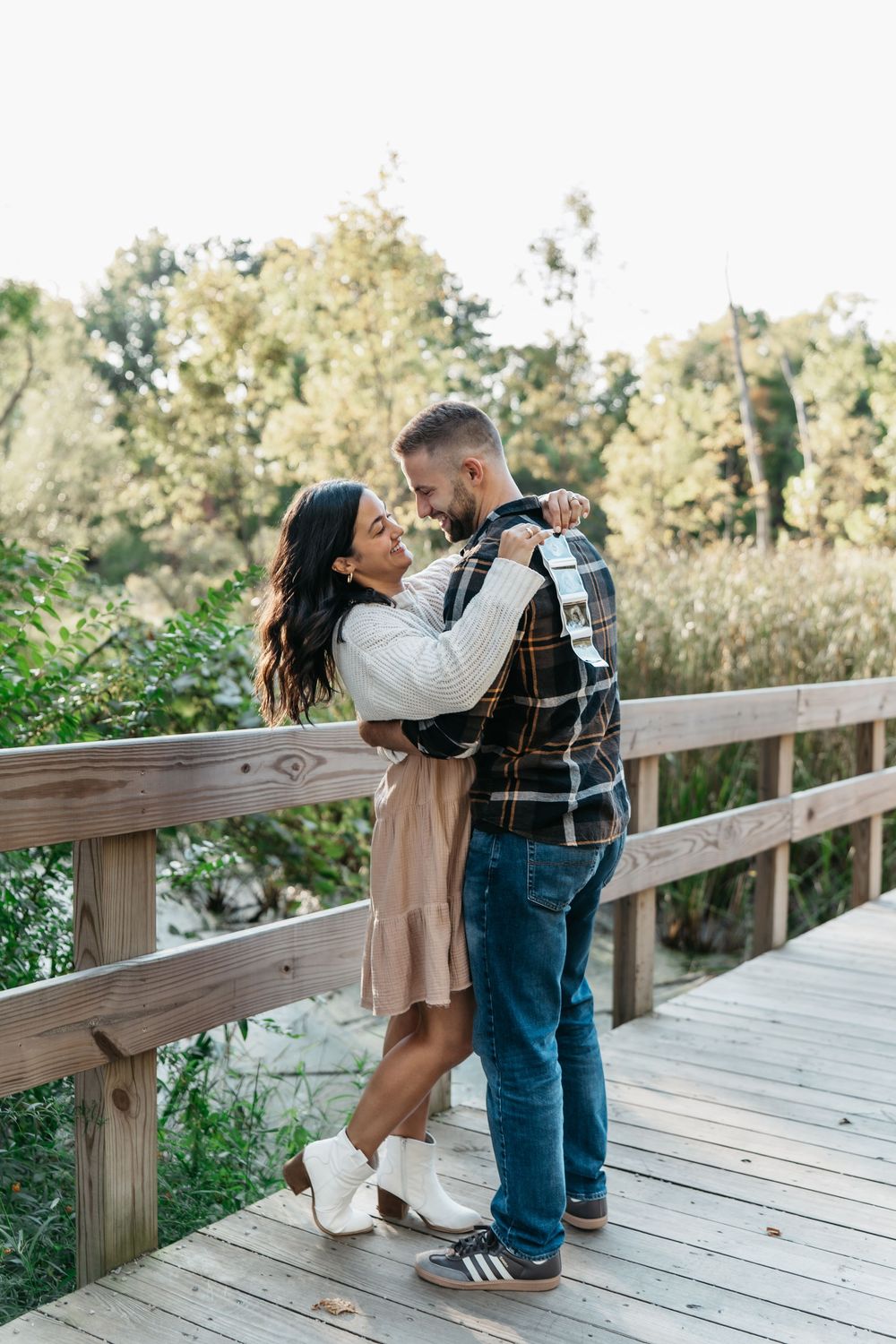 A romantic couple embraces on a bridge by lush greenery on a sunny afternoon in Cuyahoga Falls Ohio for pregnancy announcement photo session