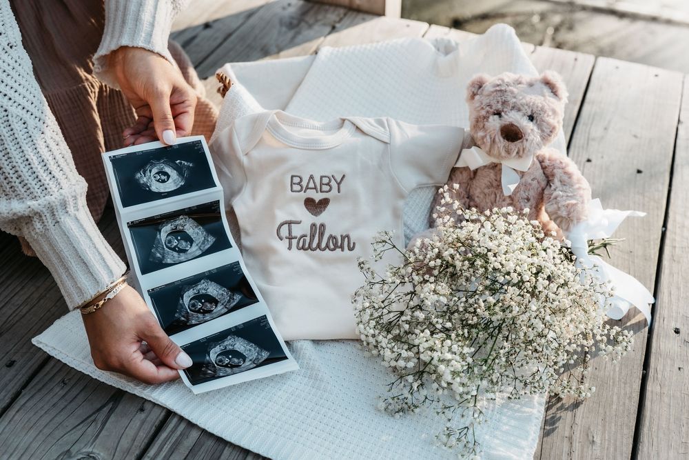Hands holding ultrasound photos and baby's breath flowers arranged on a white surface with soft natural lighting for pregnancy announcement