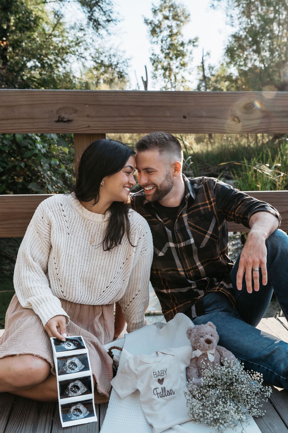 A couple sits outdoors with their small dog and ultrasound photos, sharing a tender pregnancy announcement photo session in Cuyahoga Falls