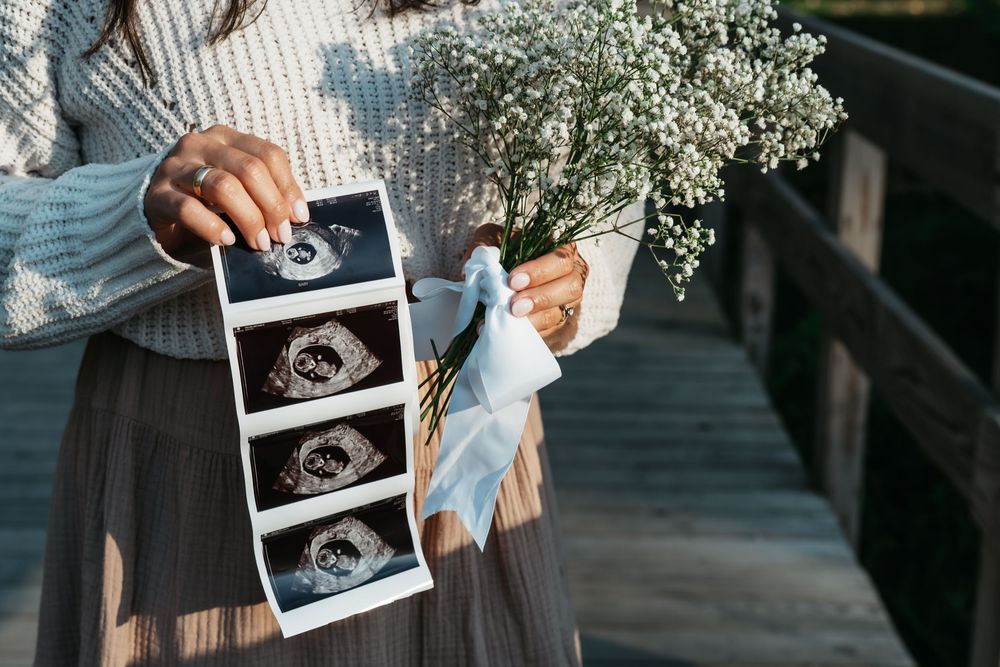 Someone holds up a black and white ultrasound photo against a floral backdrop in Cuyahoga Falls, Ohio Mud Brook Greenway Trail for Pregnancy