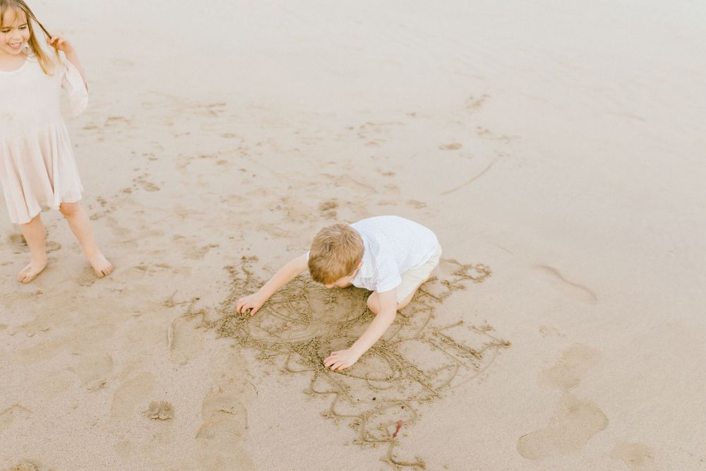 People in white clothing walk along a sandy beach shoreline while leaving footprints in the wet sand.