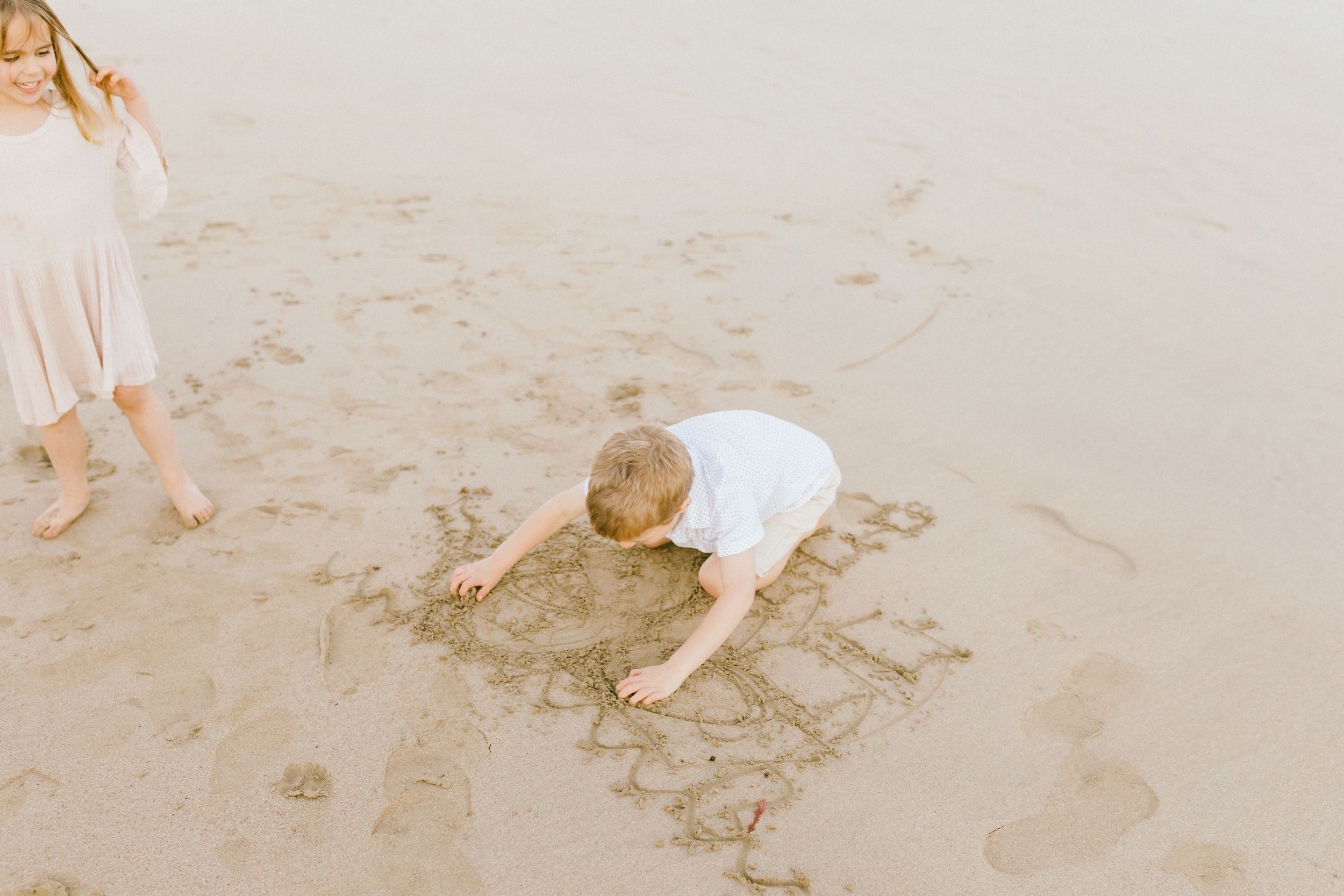 People in white clothing walk along a sandy beach shoreline while leaving footprints in the wet sand.