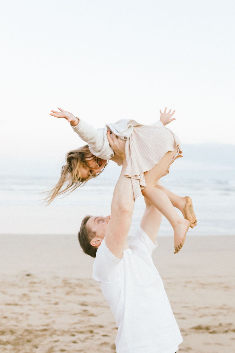 A series of photos showing a parent in white clothing lifting and playing with a child on a sandy beach.