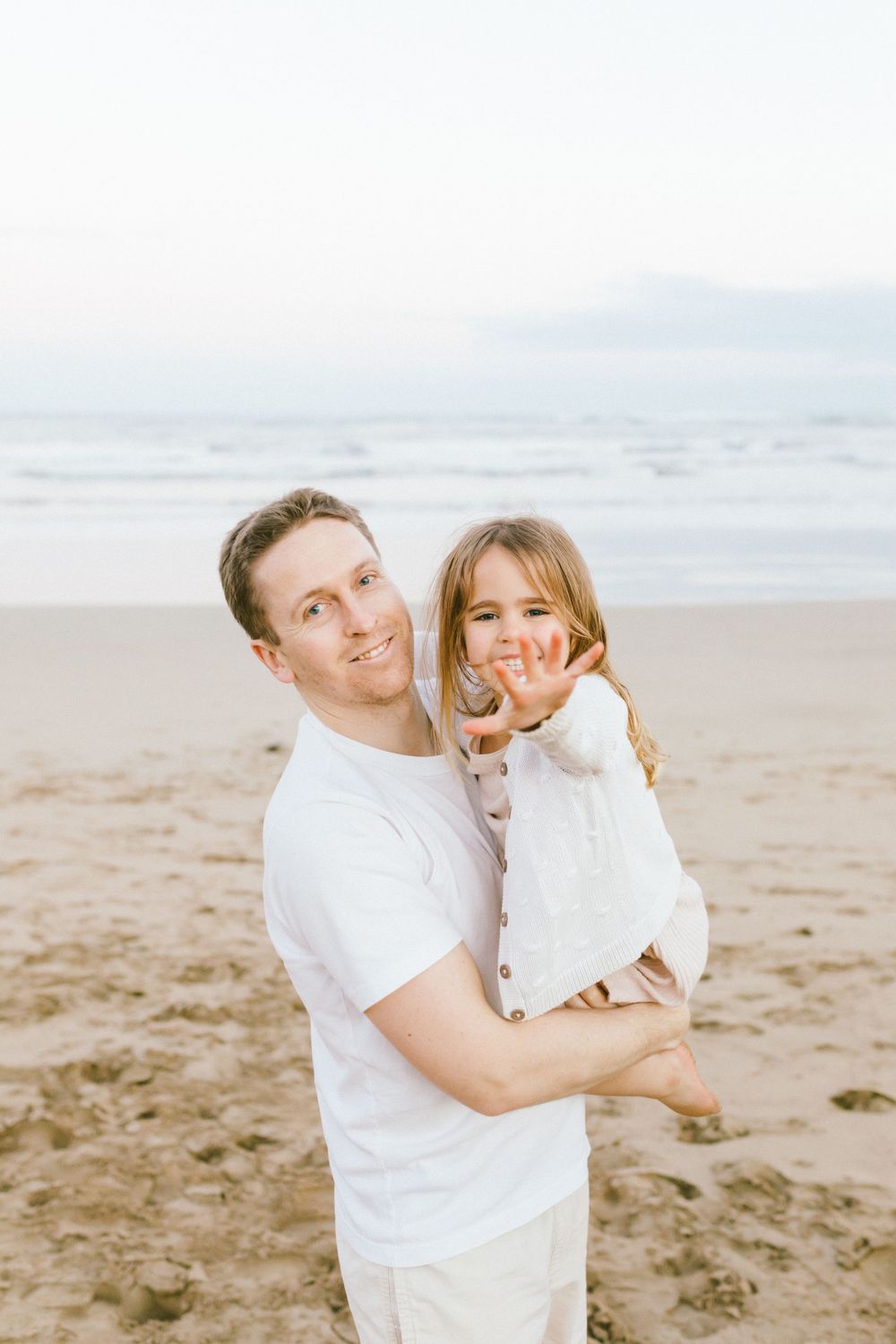 A couple in white outfits shares joyful moments together on a sandy beach during a photo session.