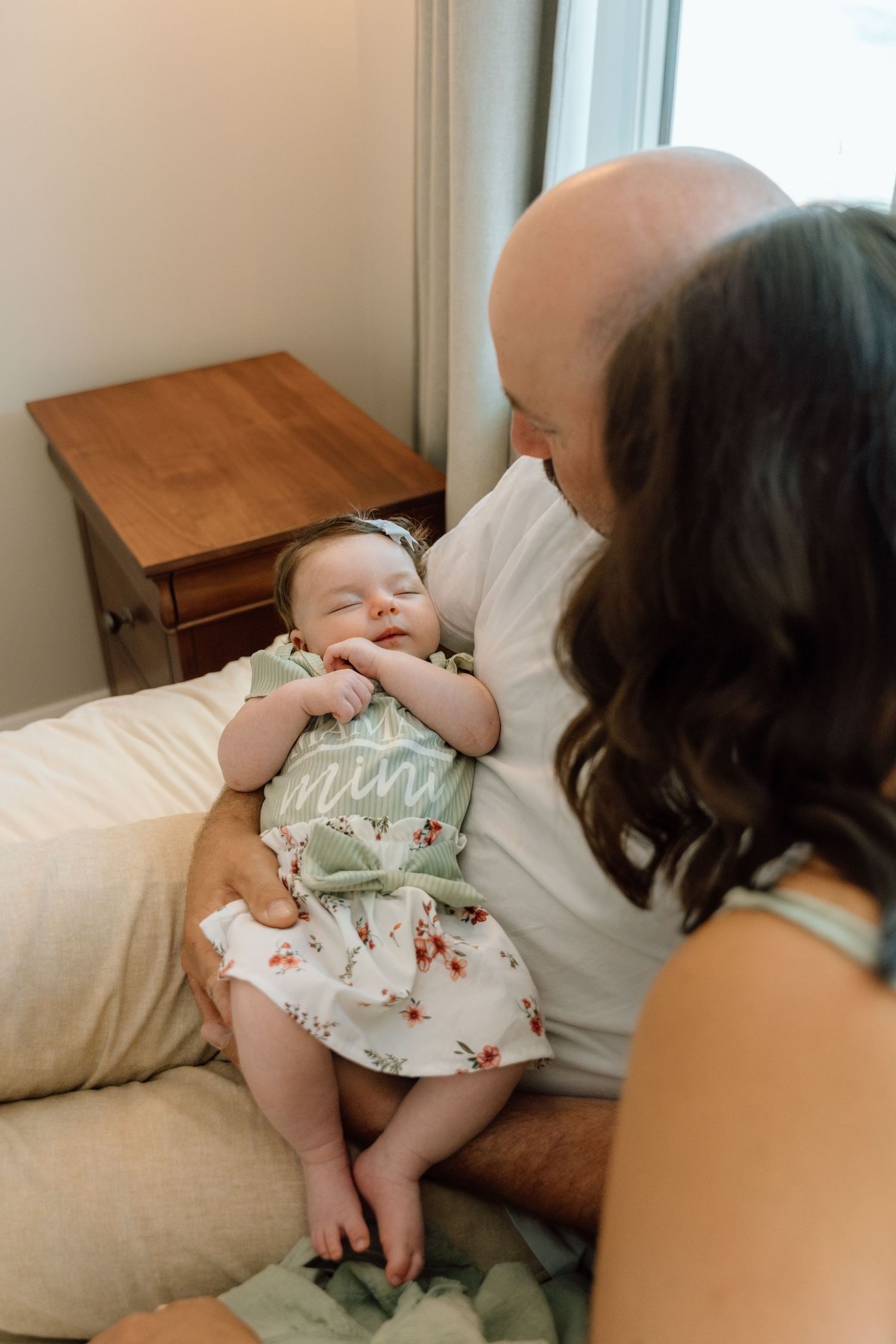 Baby in floral dress lies on couch while being tickled and laughing during playful moment.