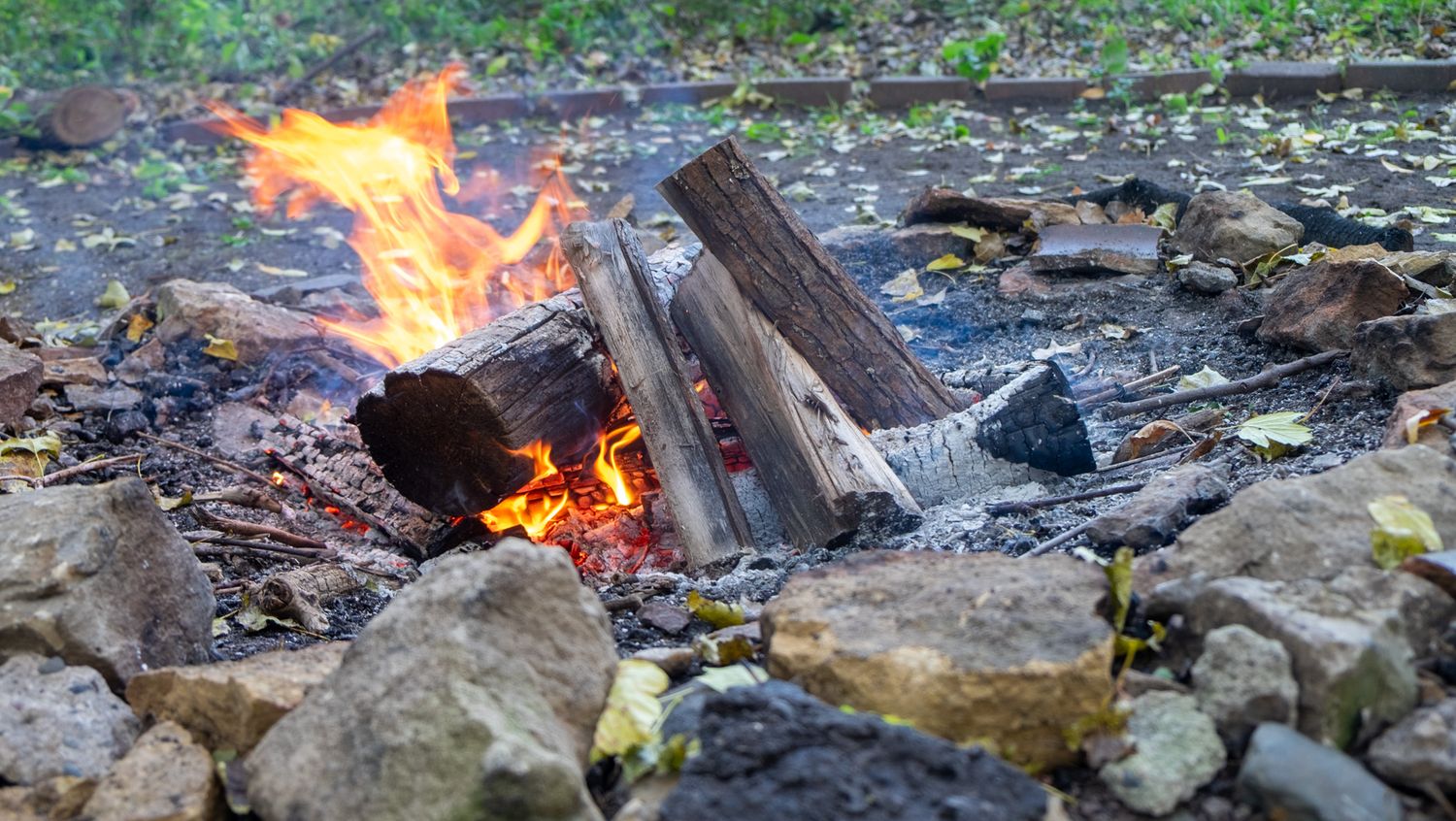 A series of campfire flames burning brightly against rocks and forest debris in an outdoor setting.