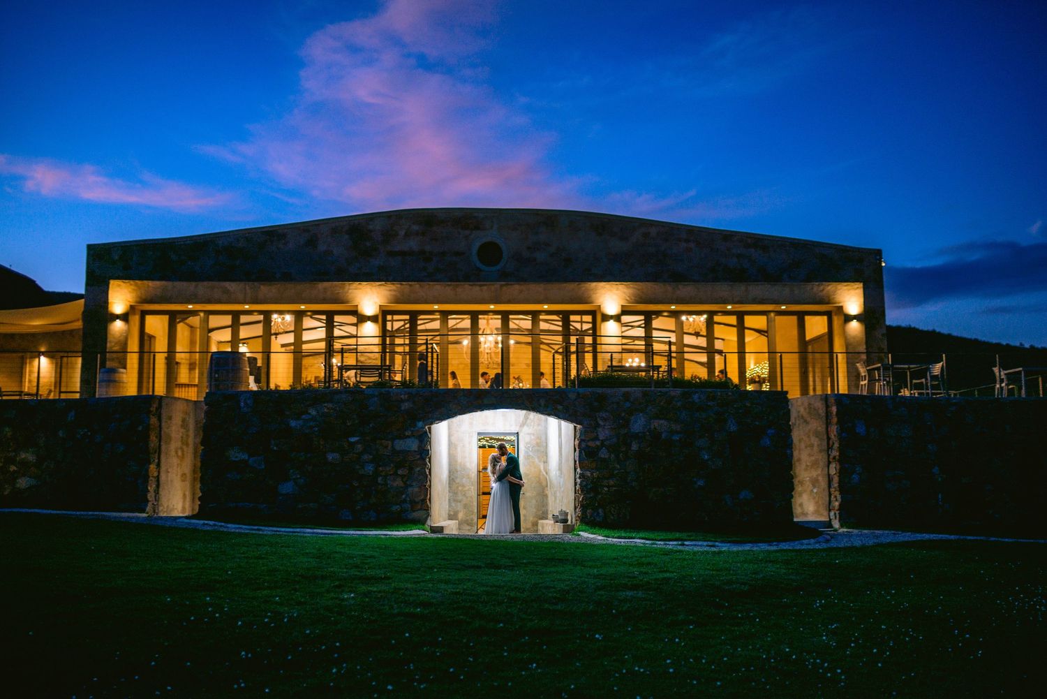 Modern architectural building with glass walls illuminated at dusk against a deep blue evening sky.