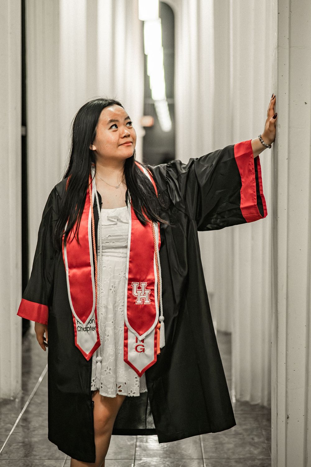 Graduate in black and red academic regalia poses dramatically against white pillars in a series of celebratory shots.