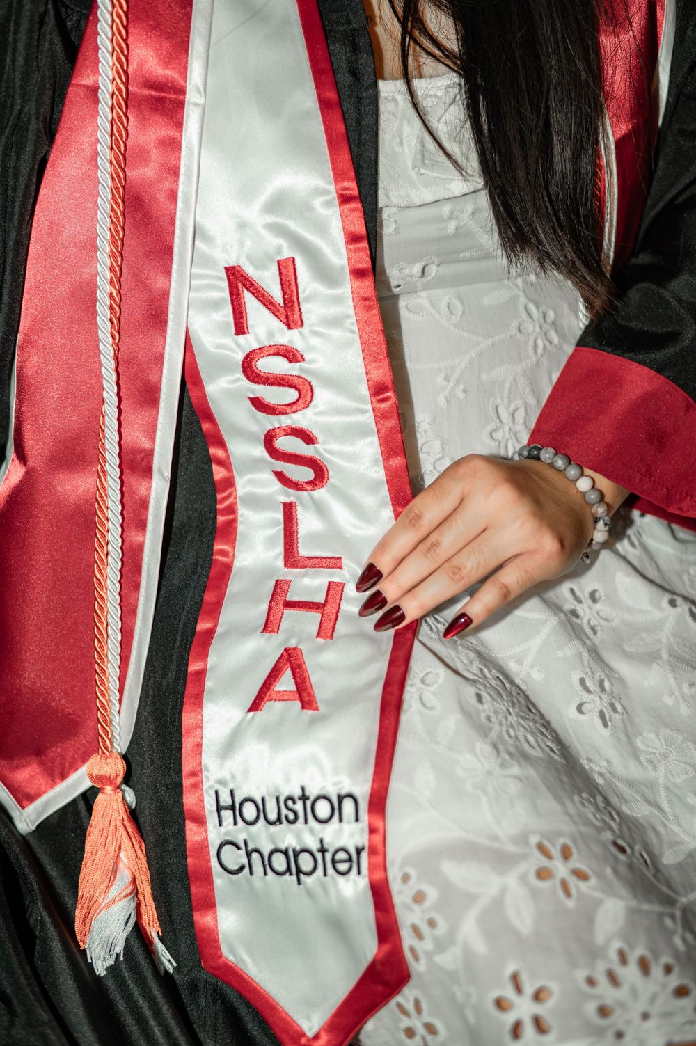 A graduation stole displaying NSSLHA Houston Chapter in red and white colors with a manicured hand visible.