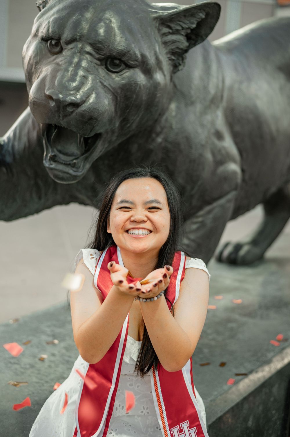 A joyful graduate poses with a large panther statue on campus during graduation celebrations.