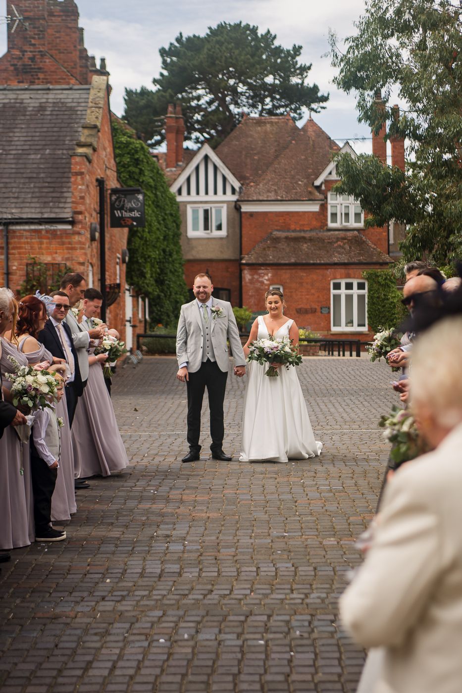 Wedding party stands on cobblestone courtyard with red brick building backdrop.