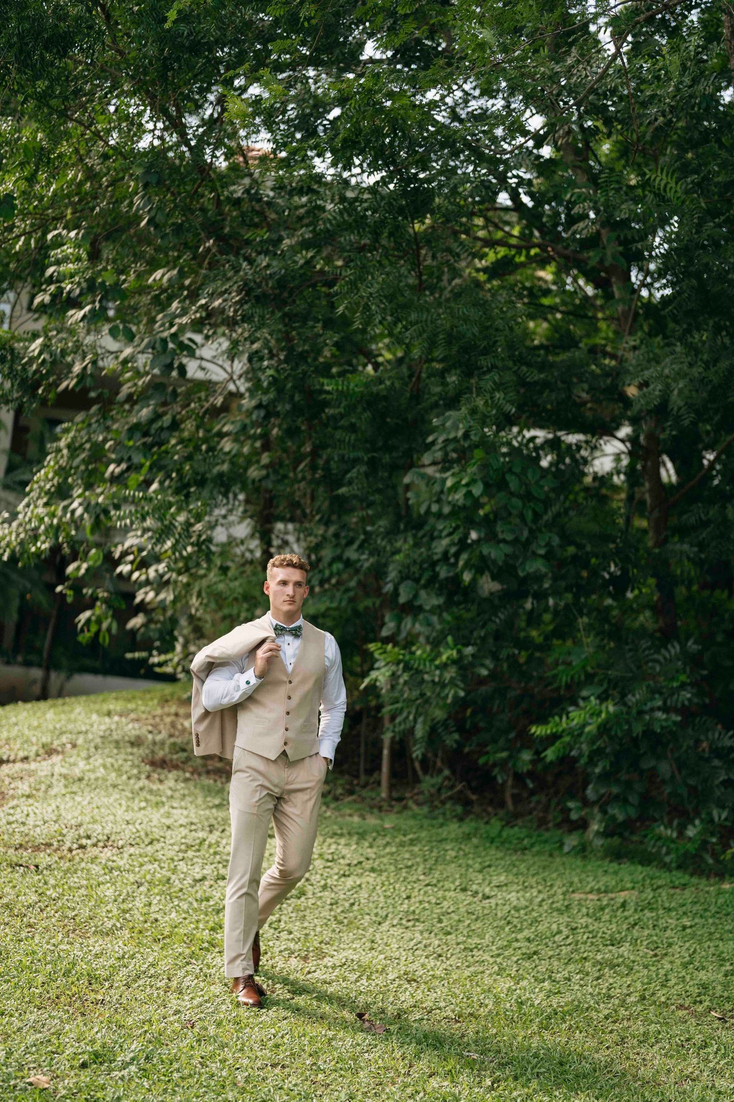 The groom playful poses on a grassy hillside surrounded by green trees in the westin conchal